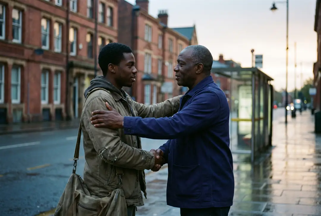 On a red-brick city street at dawn, an older Black man greets a young Black man carrying a holdall, one hand on his shoulder.